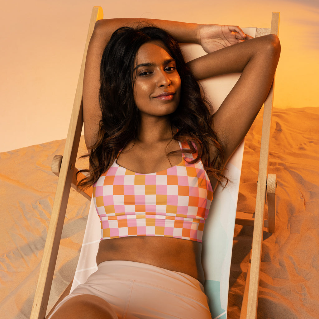 A woman wearing a women’s pink and peach checkered buttery soft recycled longline sports bra with high intensity support