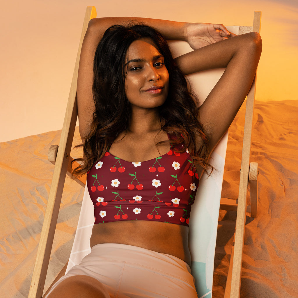 A maroon buttery soft recycled longline sports bra with cherry print offering high intensity support and quick dry features