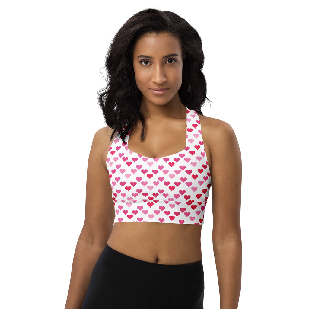 A white longline sports bra with pink and red heart pattern made from buttery soft recycled fabric for high intensity support