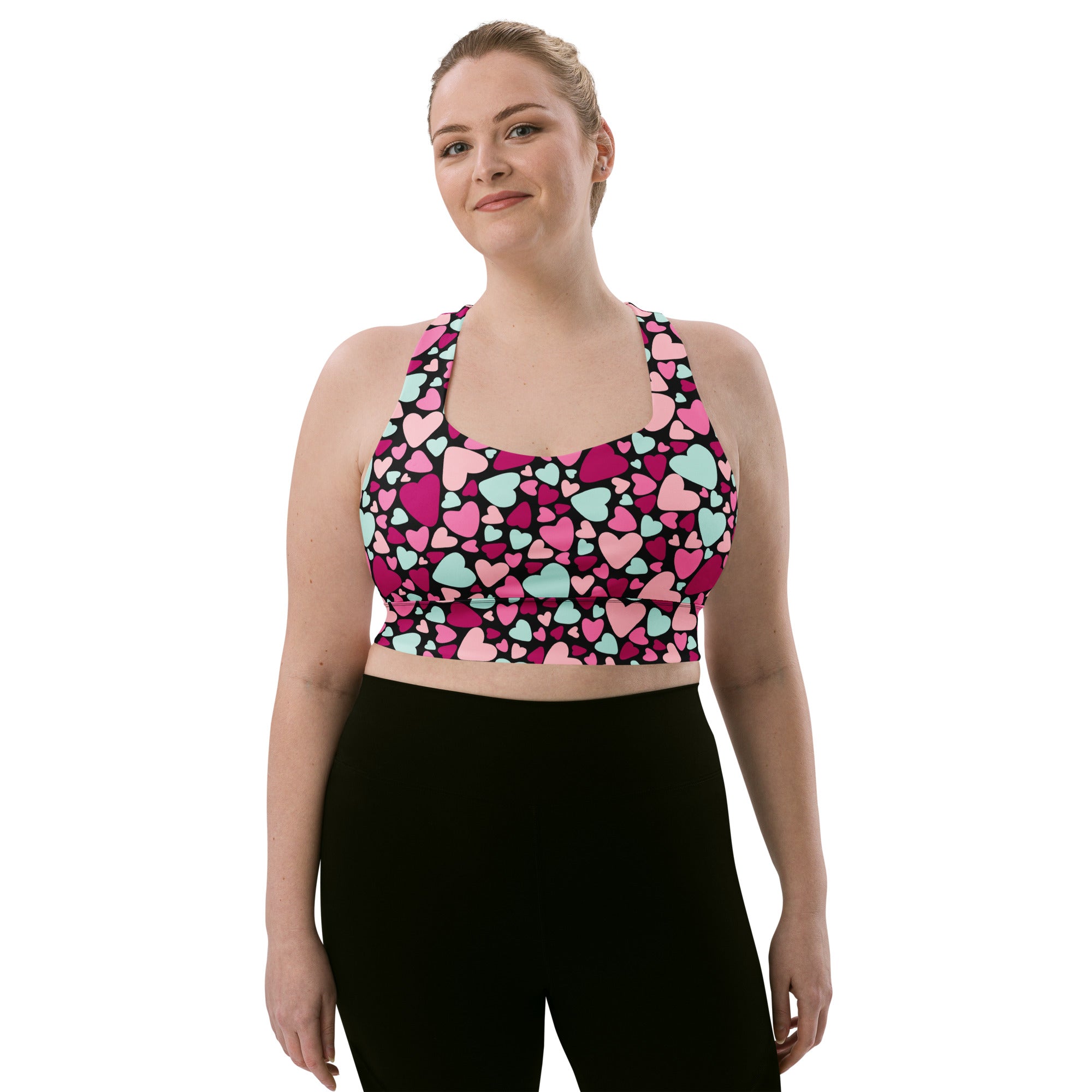 A vibrant women’s valentine’s day longline sports bra with pink magenta and mint hearts on black buttery soft recycled fabric