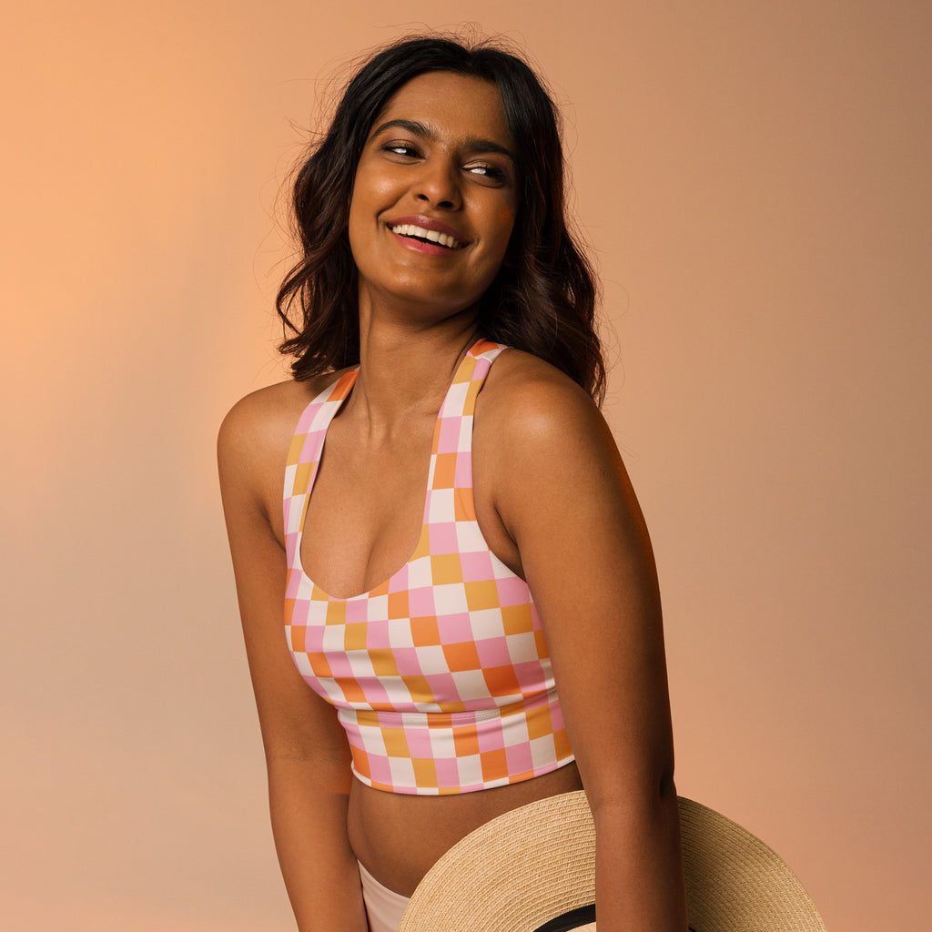 A vibrant pink and orange checkered buttery soft recycled longline sports bra with halter neck straps and high support