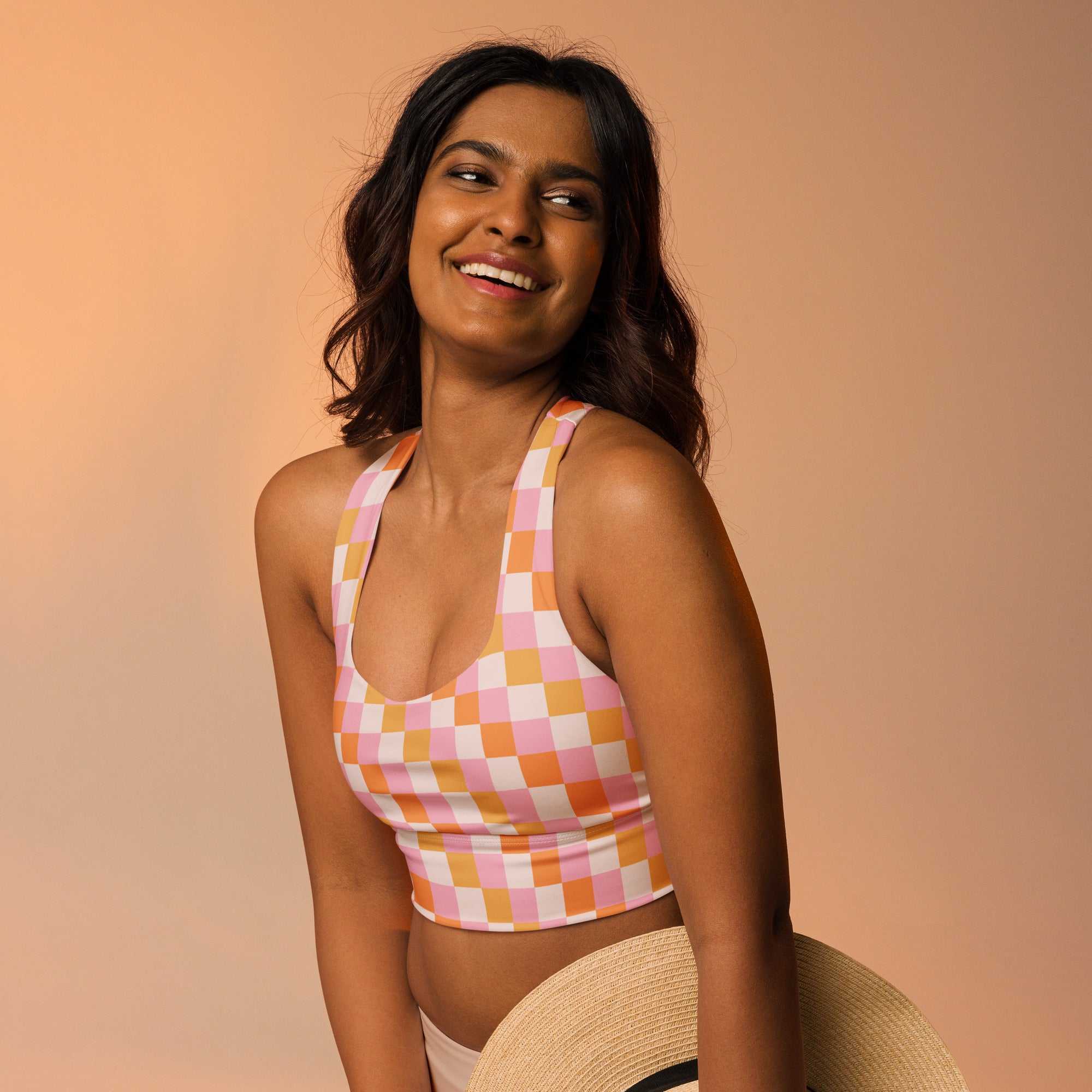 A vibrant pink and orange checkered buttery soft recycled longline sports bra with halter neck straps and high support