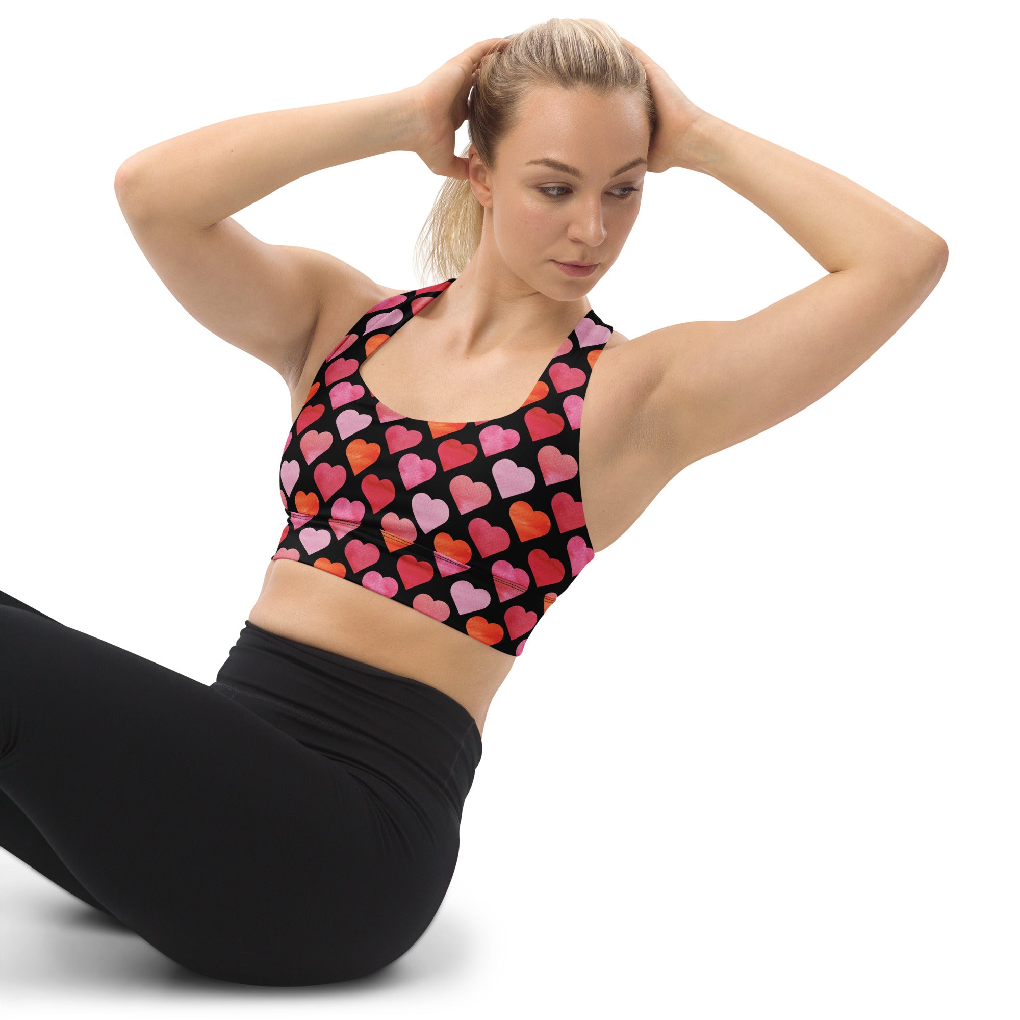 A black longline sports bra with vibrant pink and orange hearts featuring high intensity support and buttery soft recycled fabric