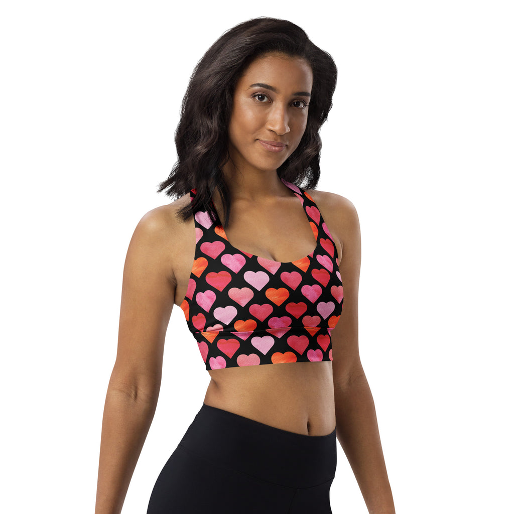 Women’s black longline sports bra with vibrant pink and orange heart print made from buttery soft recycled fabric