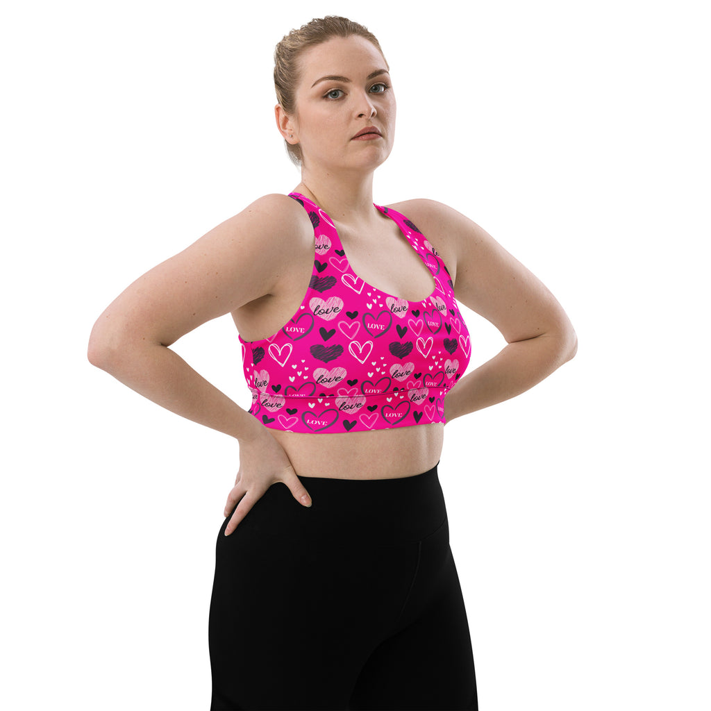 A vibrant pink longline sports bra with black and white love heart pattern made from buttery soft recycled fabric