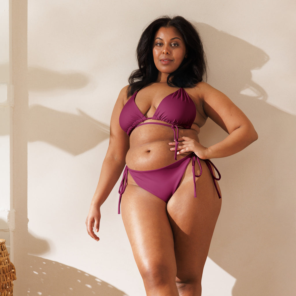 A plus-size woman wearing a vibrant magenta purple buttery soft recycled string bikini with adjustable tie-side strings and UPF 50+