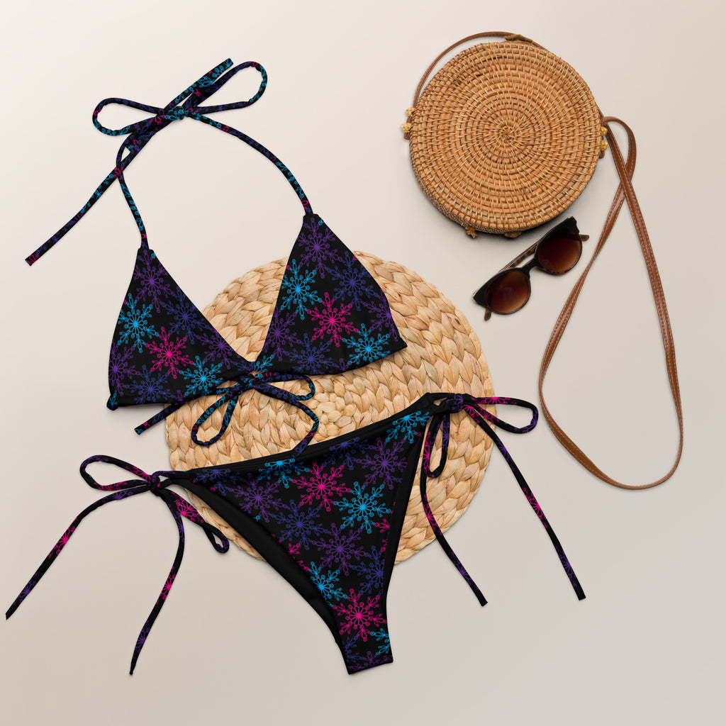 A vibrant dark navy buttery soft recycled string bikini with neon blue and magenta snowflake patterns and UPF 50+