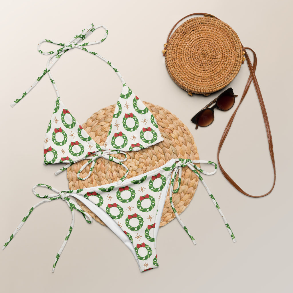 White bikini set with green and red christmas wreath patterns made of buttery soft recycled fabric with upf 50+ on woven mat