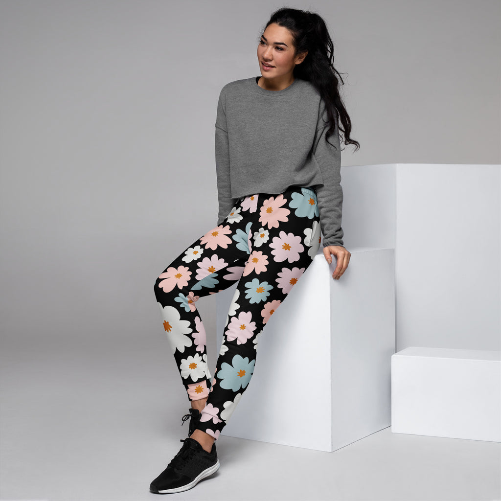 Women’s retro floral recycled jogger pants with pockets in black featuring vibrant pink white and light blue daisy pattern