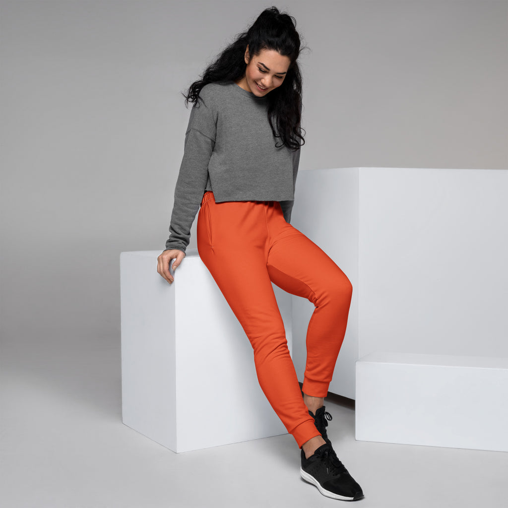 A woman wearing women’s orange recycled jogger pants with cozy brushed inside fleece and pockets paired with a gray cropped sweatshirt
