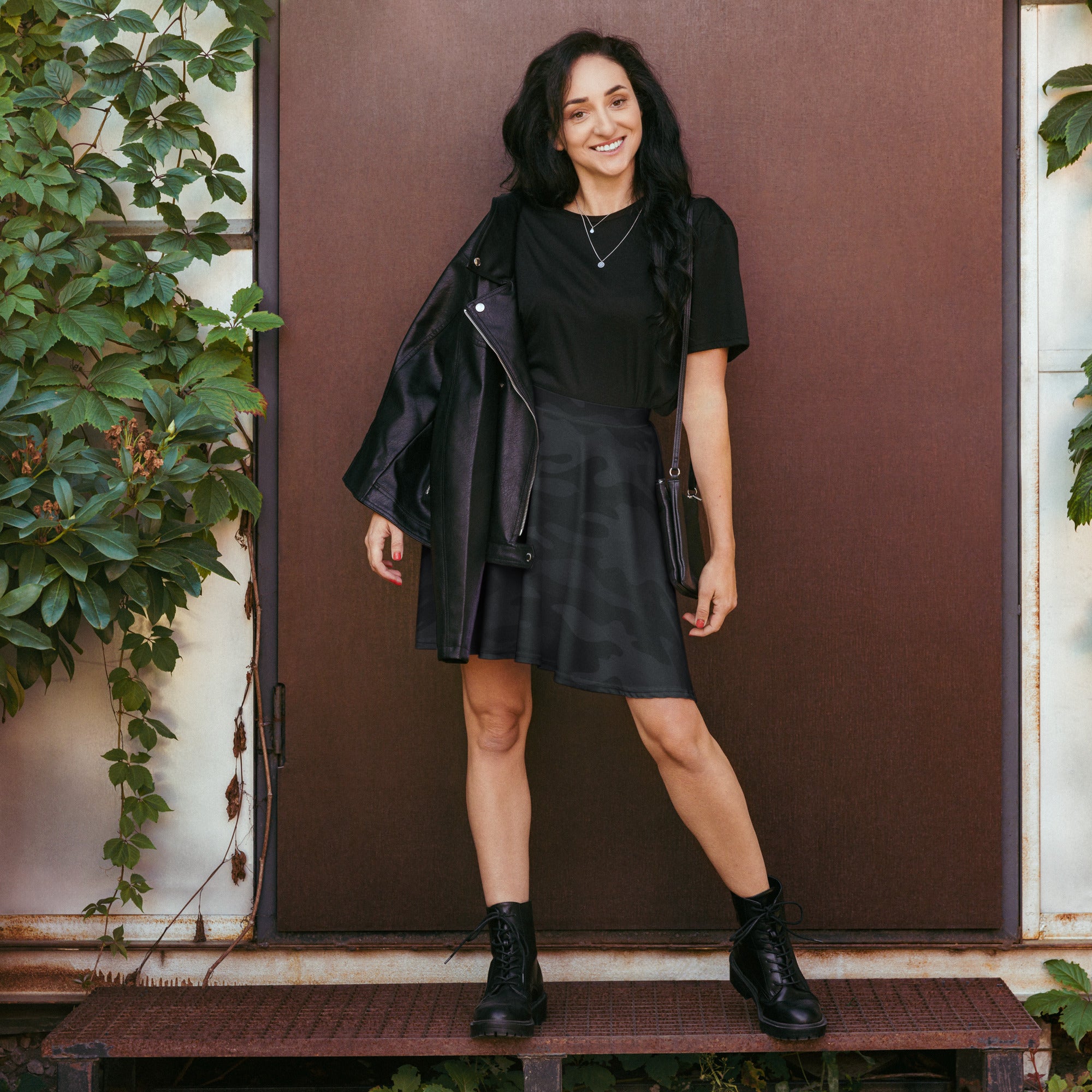 Women’s black leather jacket with zipper details paired with black camouflage skater skirt with upf 50 plus recycled fabric
