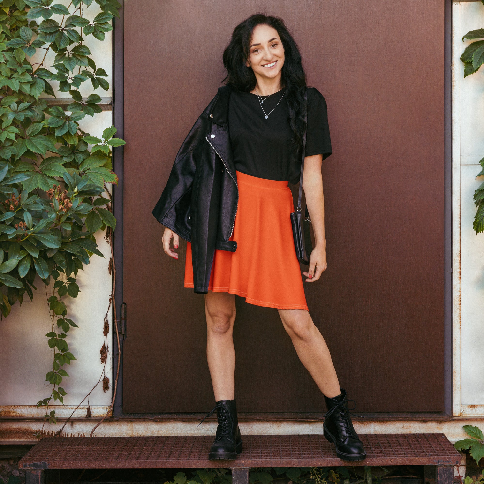 Black leather jacket with zipper details and collar paired with women’s bright orange high waisted skater skirt with upf 50 and recycled fabric