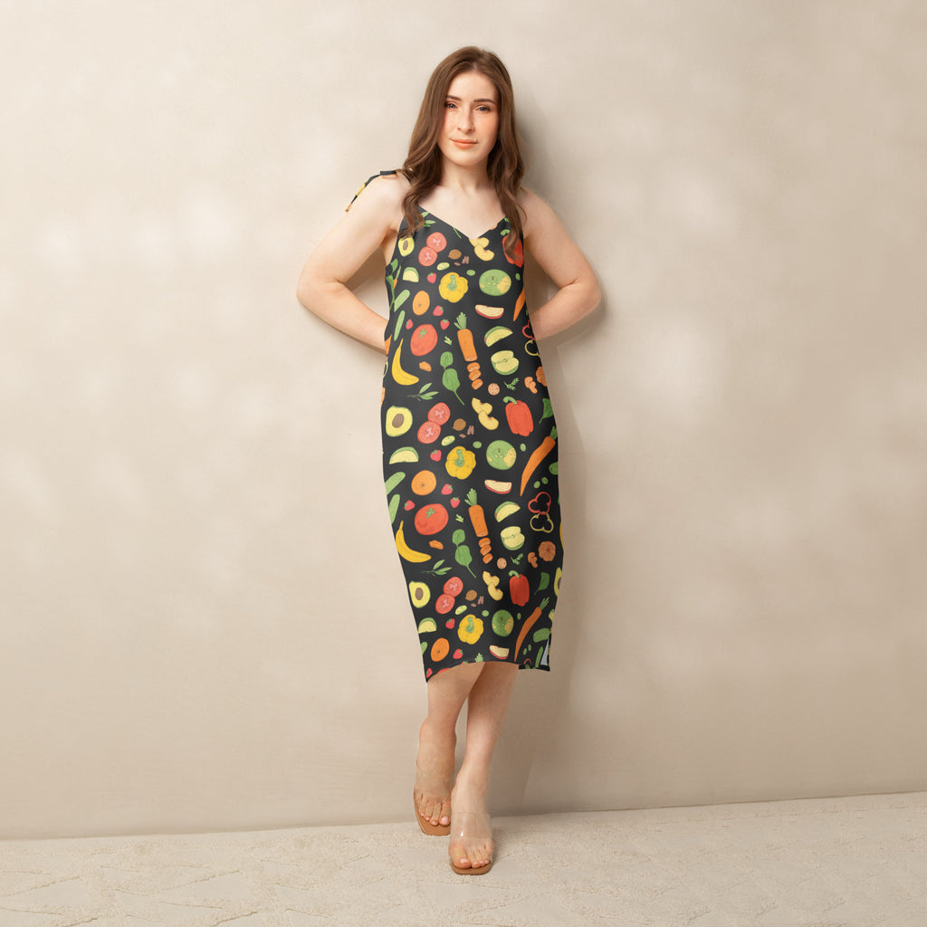 A black sleeveless midi slip dress with vibrant fruit and vegetable pattern, adjustable tie straps, and built-in bra