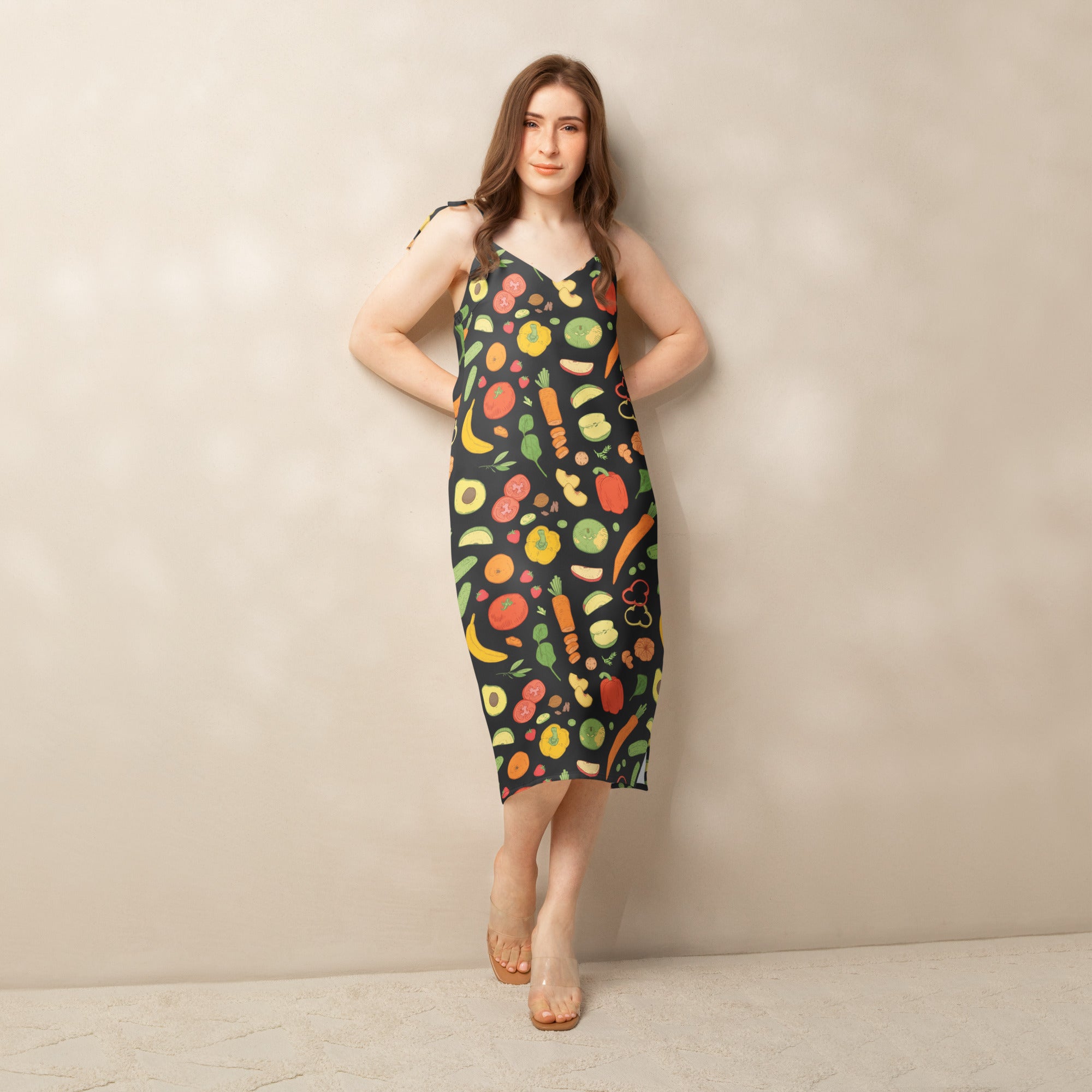 A black sleeveless midi slip dress with vibrant fruit and vegetable pattern, adjustable tie straps, and built-in bra