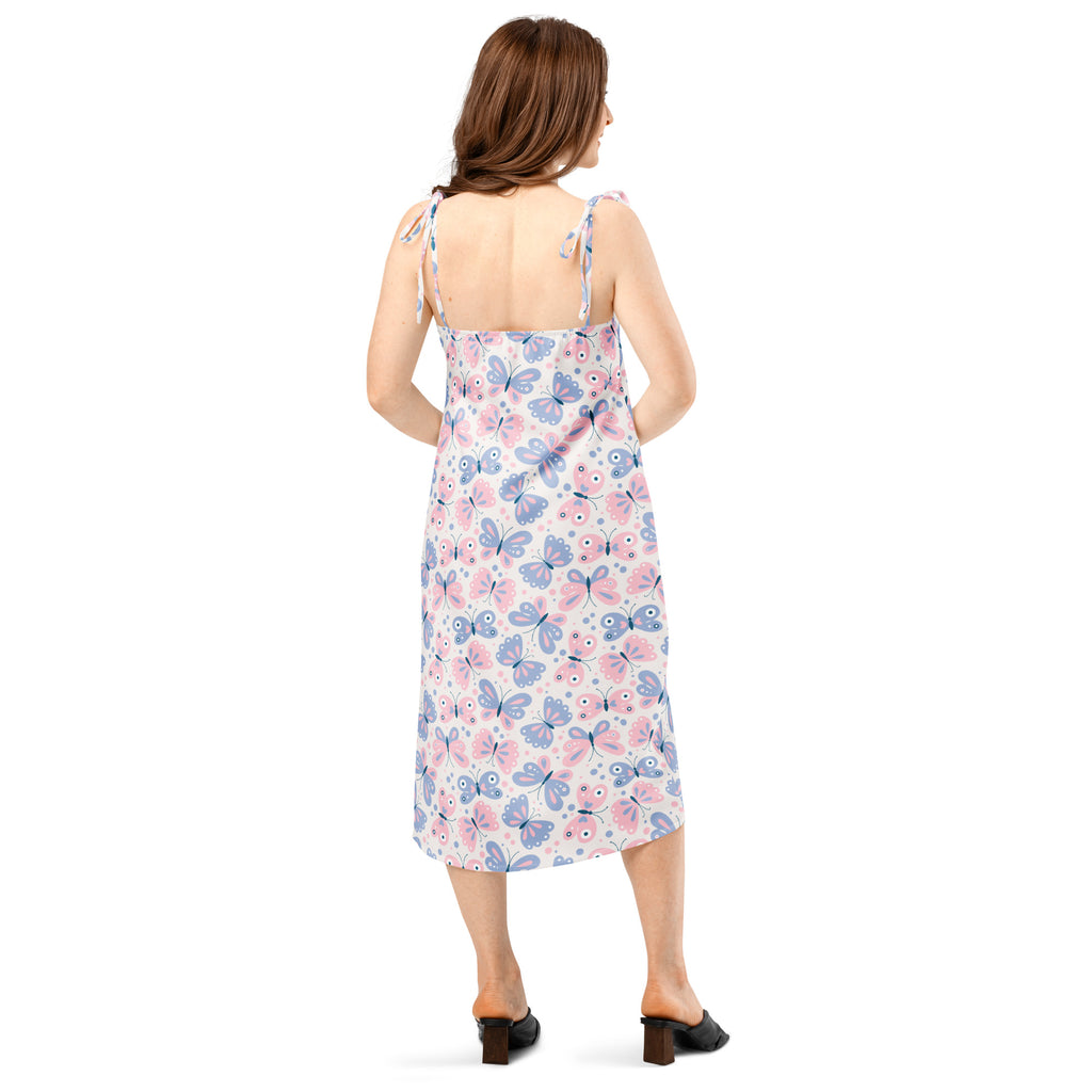 A woman wears a light-colored midi slip dress with pink and blue butterfly print and adjustable tie straps