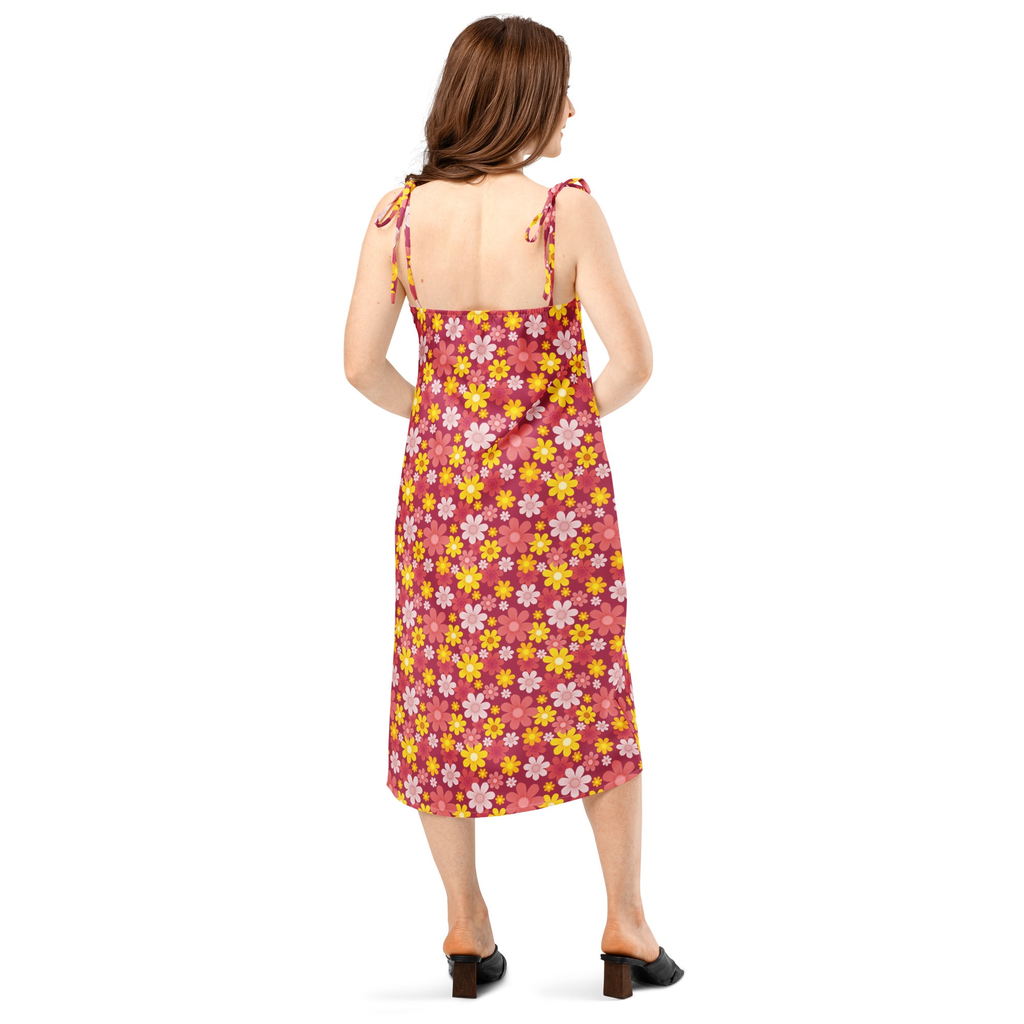 A woman wears a vibrant pink floral midi slip dress with yellow and white blossoms and adjustable tie straps
