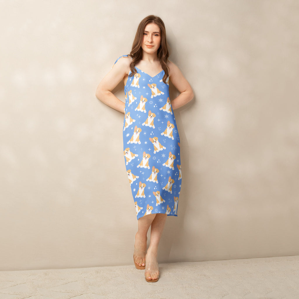 A blue sleeveless midi slip dress with adjustable tie straps featuring a playful corgi dog and snowflake pattern