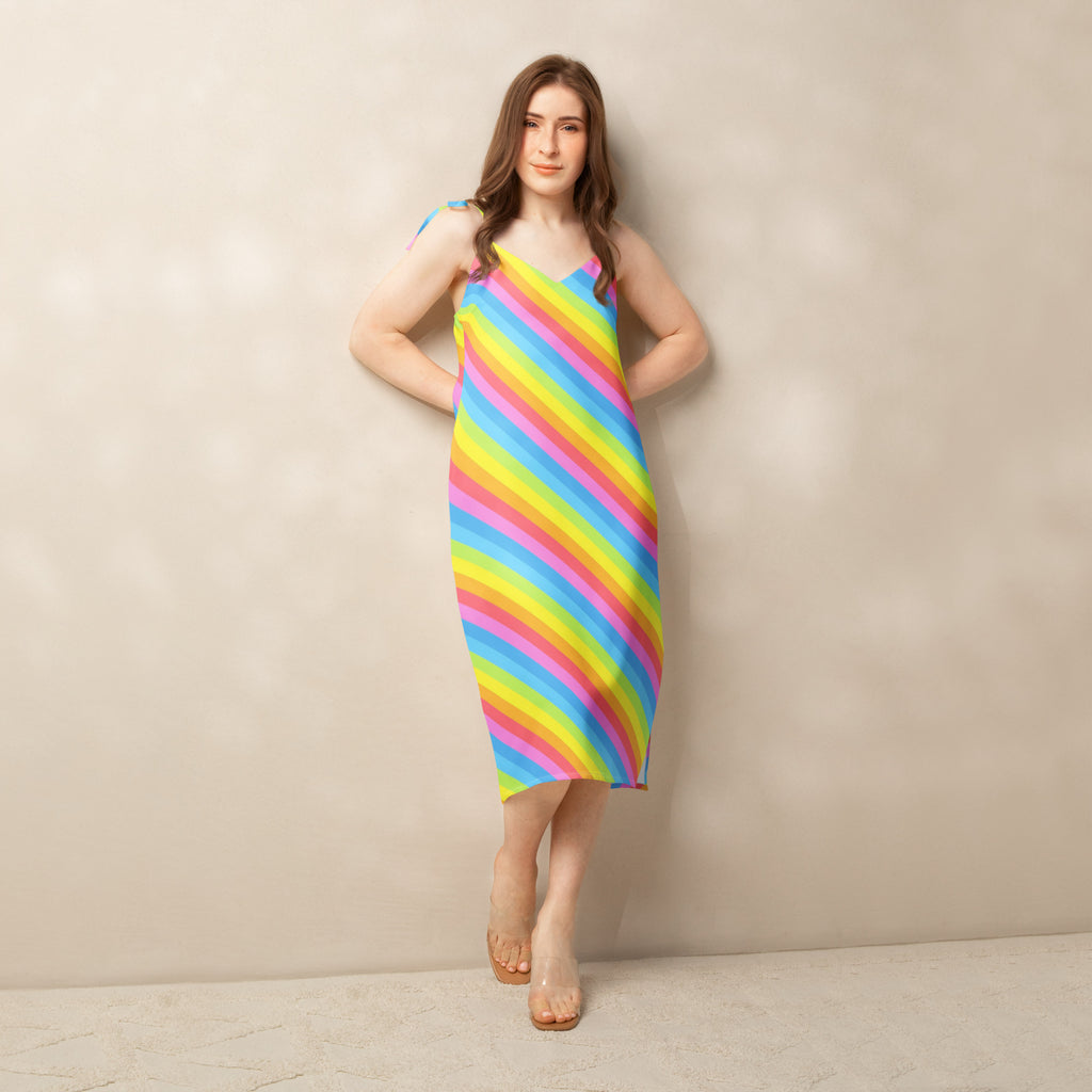 A vibrant knee-length women’s rainbow stripe slip dress with adjustable tie straps and built in bra features diagonal pink yellow blue and green stripes