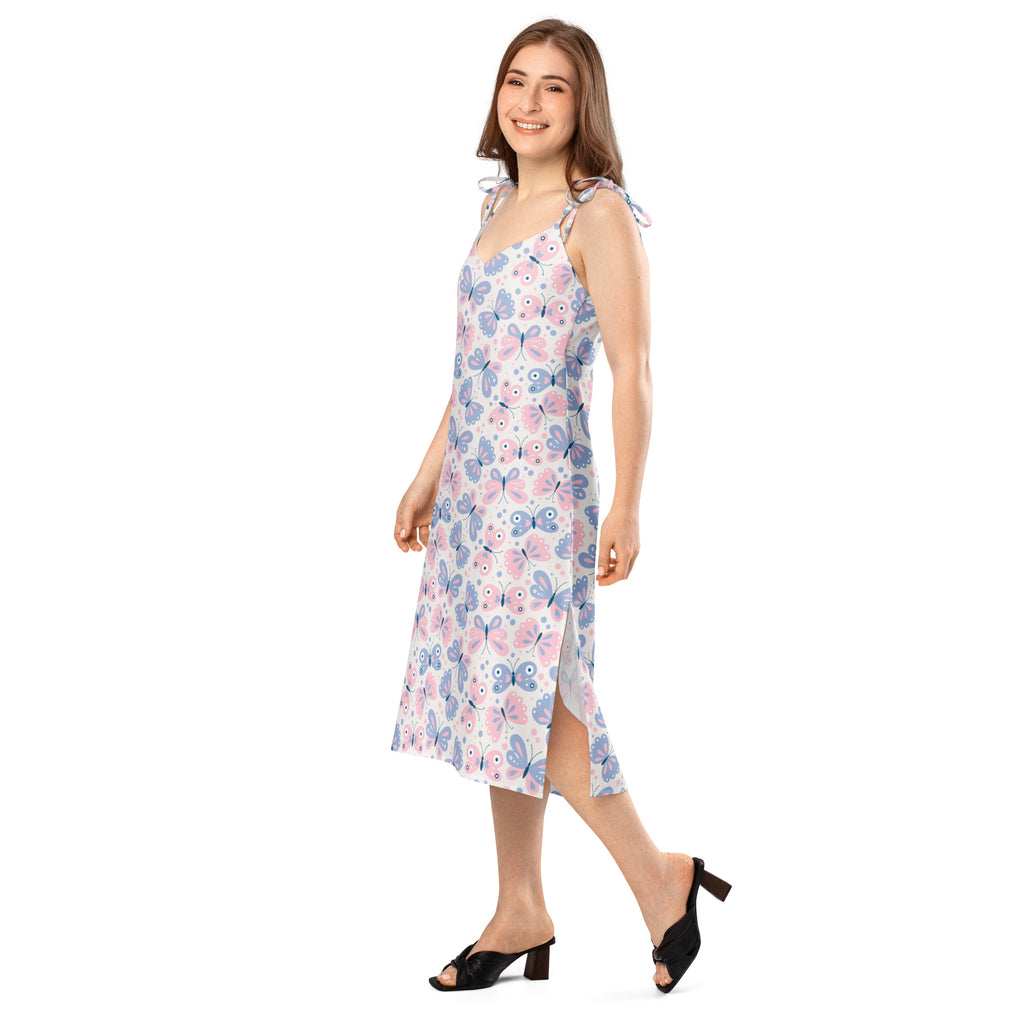 A woman wears a light pink and blue butterfly print sleeveless midi slip dress with adjustable tie straps and built in bra