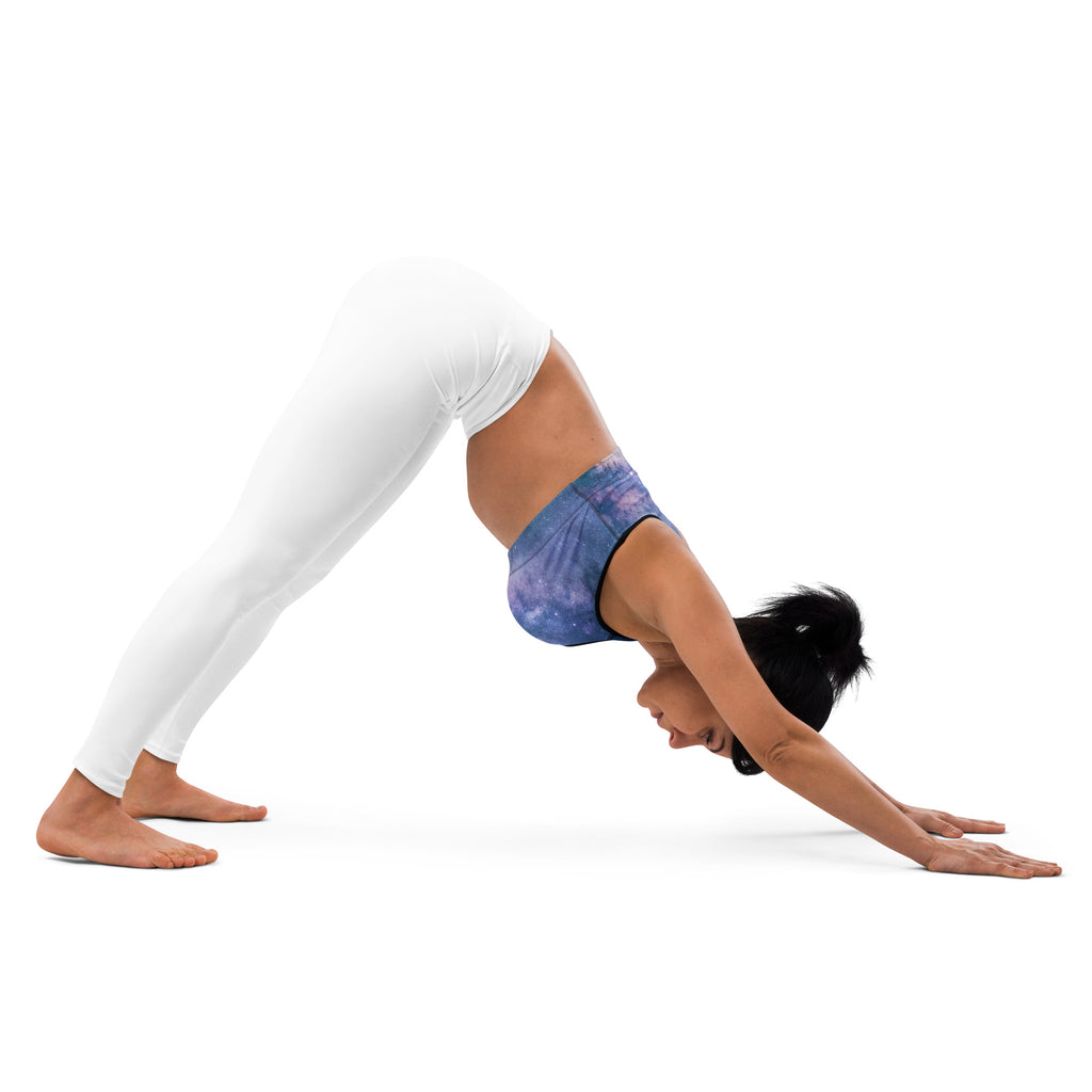 Woman in a blue galaxy quick drying sports bra and white leggings performing downward dog yoga pose