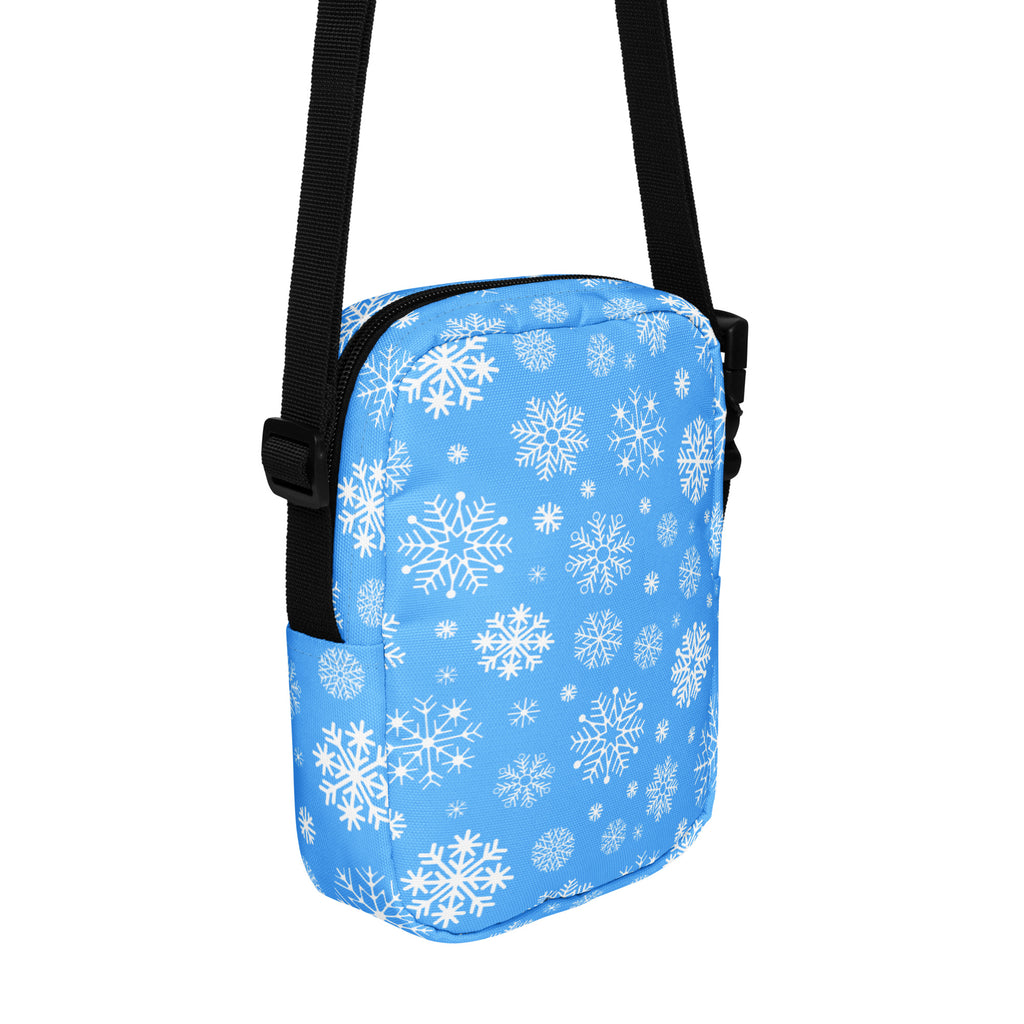 A light blue winter women’s crossbody purse with white snowflake pattern and black adjustable strap