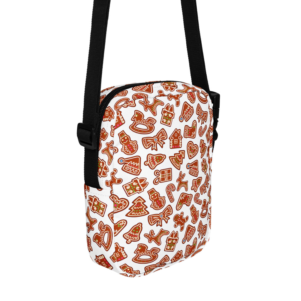 A white girls crossbody purse with gingerbread cookie pattern in brown and red with black straps