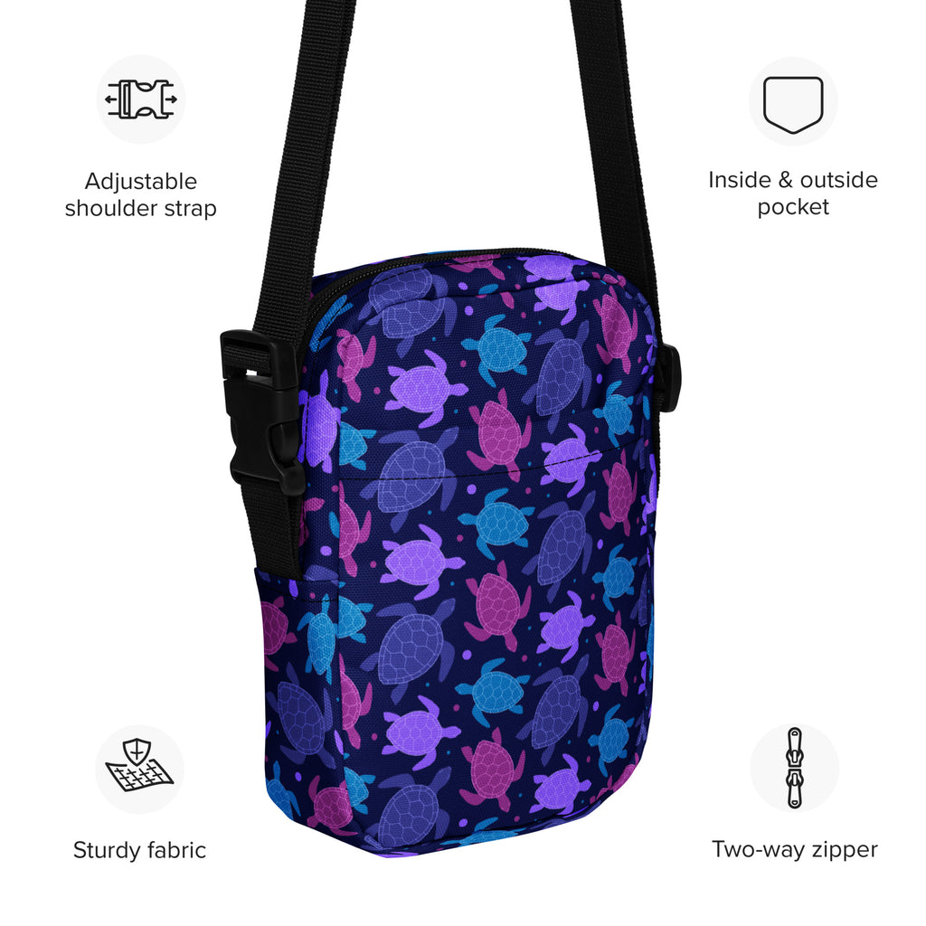 A navy blue girls crossbody purse with vibrant purple pink and teal sea turtle pattern on fabric surface