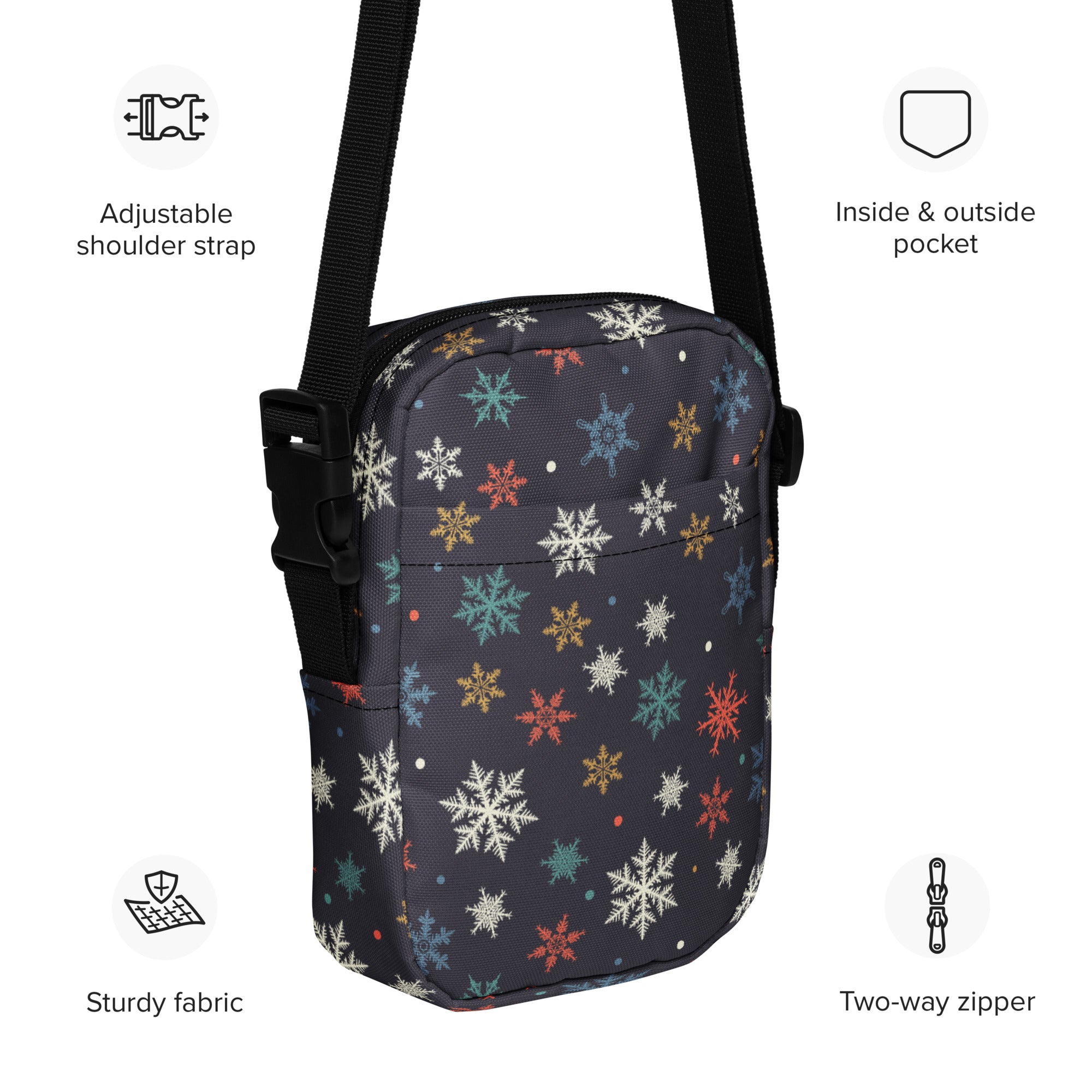 A dark gray crossbody purse with colorful snowflake patterns and black adjustable straps and zippers