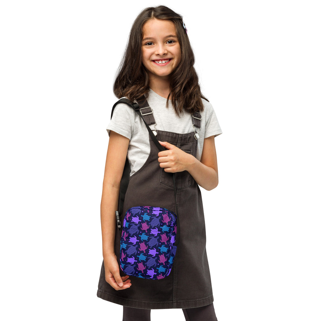 Girls purple sea turtle crossbody purse with purple and blue turtle patterned fabric attached to dark gray overalls