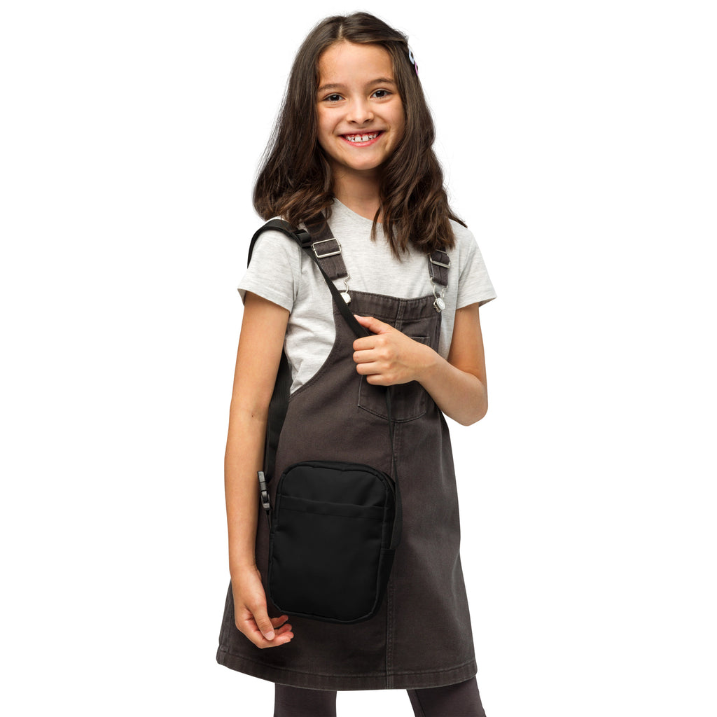 Dark gray denim overall dress with black front pocket and adjustable straps paired with girls black crossbody purse