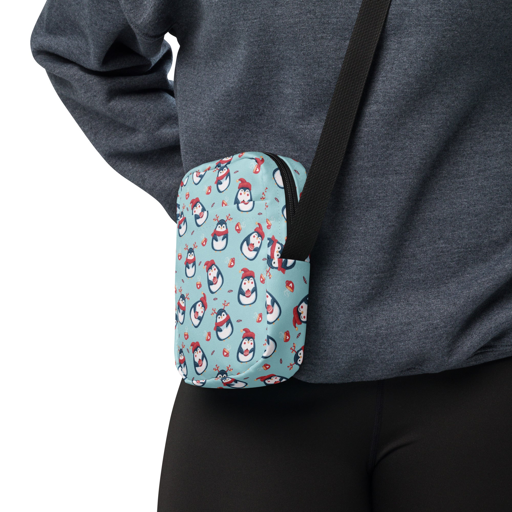 A light blue crossbody pouch with a playful pattern of cartoon penguins wearing red hats and scarves