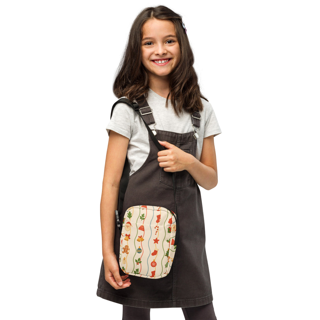 A festive cream-colored girls Christmas icons crossbody purse with holiday patterns of santa hats stockings and ornaments