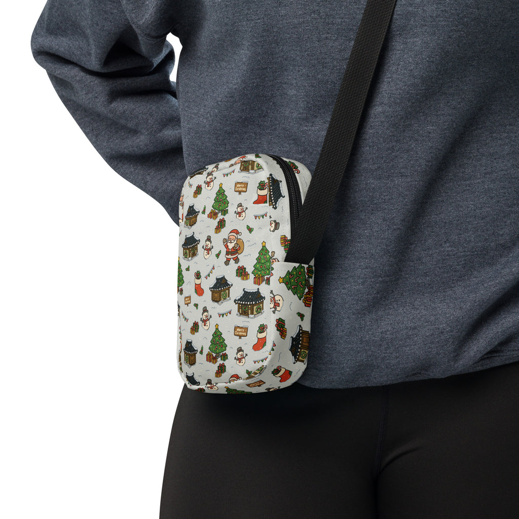 A festive white crossbody pouch featuring a holiday pattern with santa snowmen christmas trees and houses