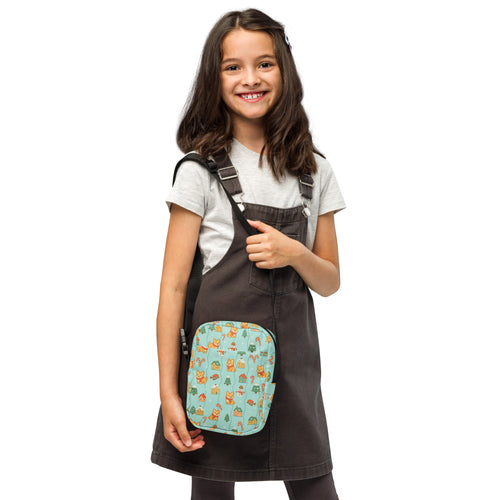 A light blue girls corgi winter wonderland crossbody purse with cartoon animals and trees worn on overalls