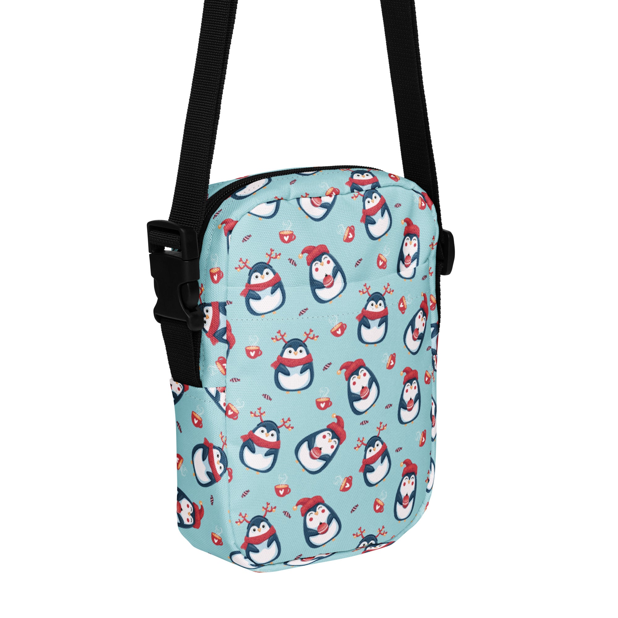 A light blue girls crossbody purse with cartoon penguins wearing red hats scarves and reindeer antlers pattern