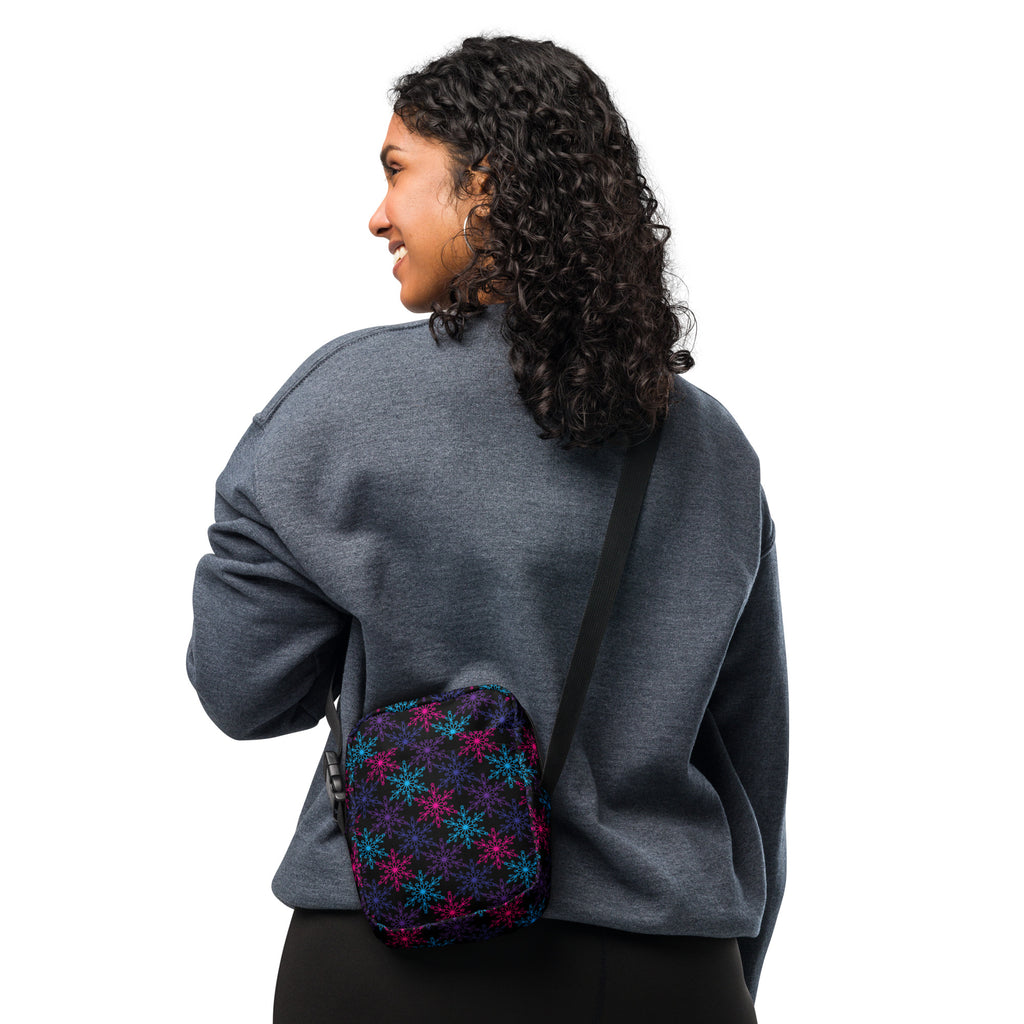 A small dark navy fabric crossbody bag with vibrant pink and blue neon snowflake patterns for winter use