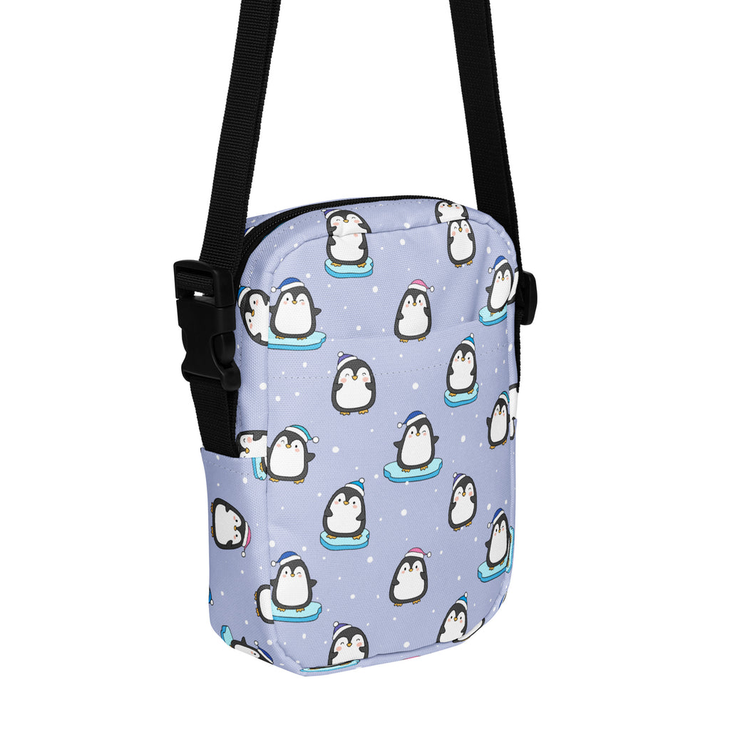 Light purple crossbody bag with playful cartoon penguins on blue skateboards against a snowy winter backdrop