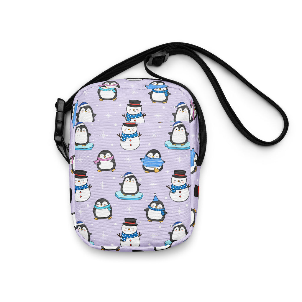 A lavender girls winter penguin crossbody purse with a playful cartoon penguin pattern wearing scarves and hats