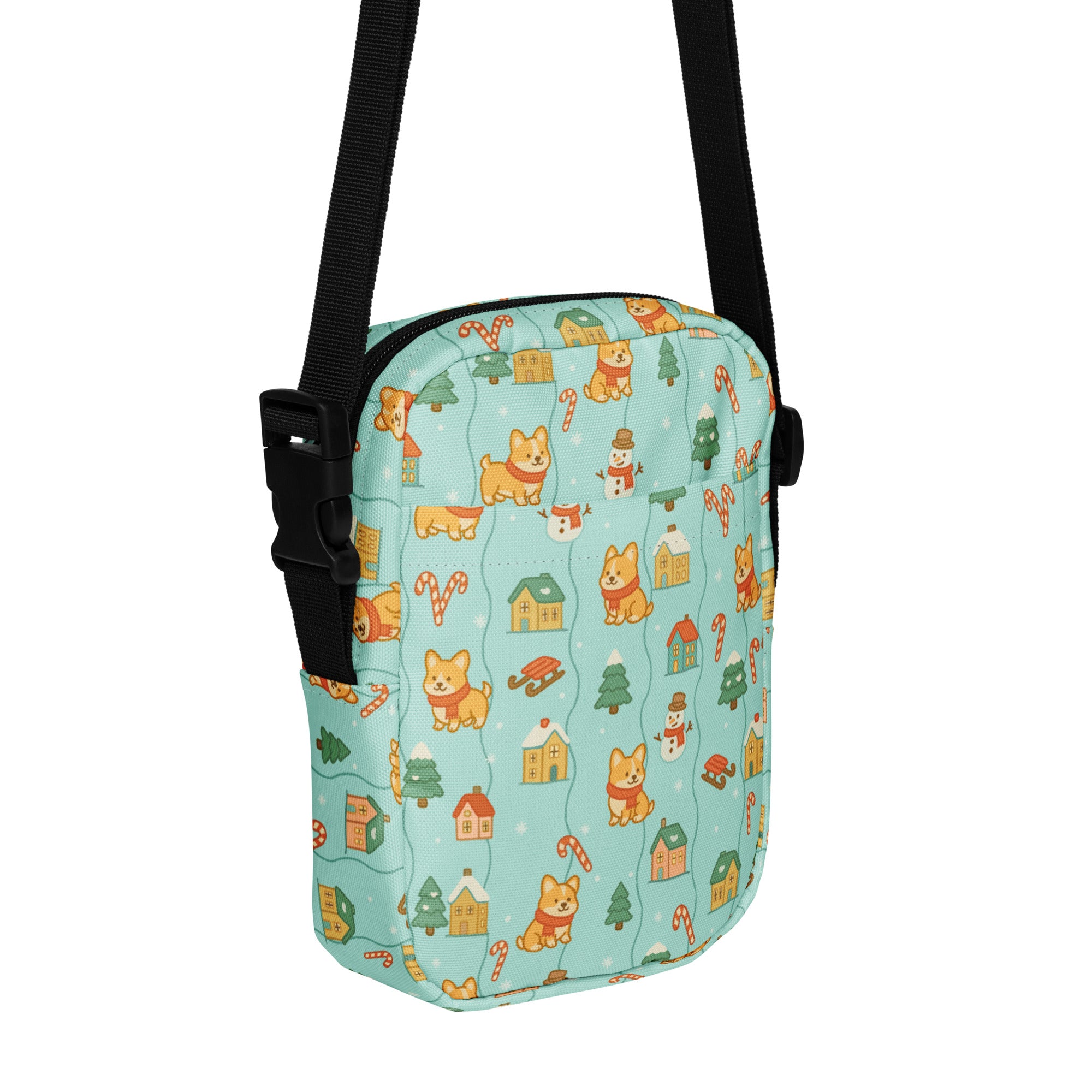 A light blue crossbody bag with a festive pattern of cartoon corgis snowmen candy canes and tiny houses