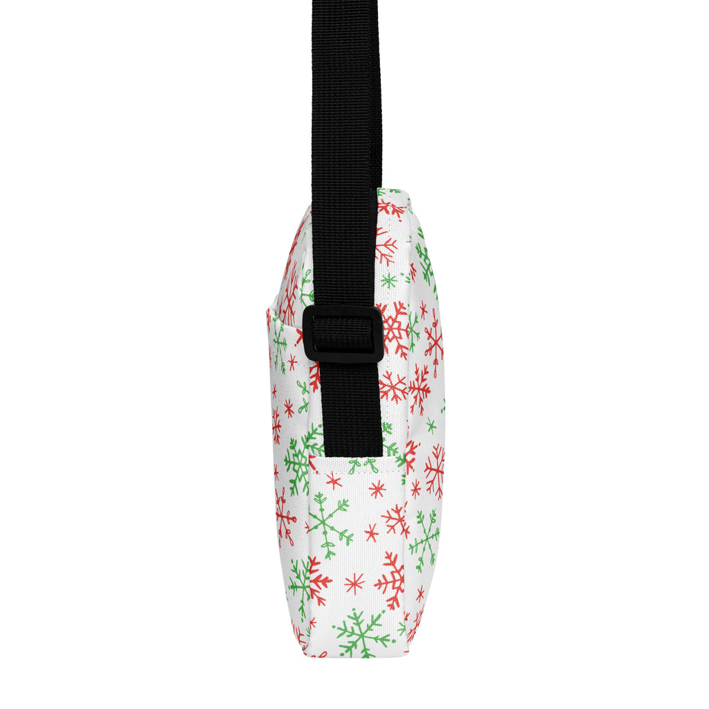 A white crossbody purse with red and green snowflake pattern and black adjustable strap for Christmas use