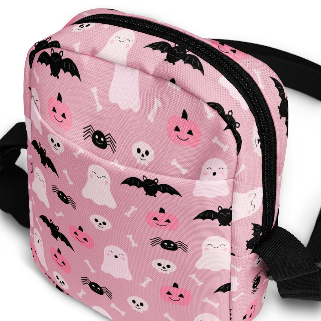 Pink halloween crossbody purse for girls with black zippers and straps featuring white and black ghost and bat patterns