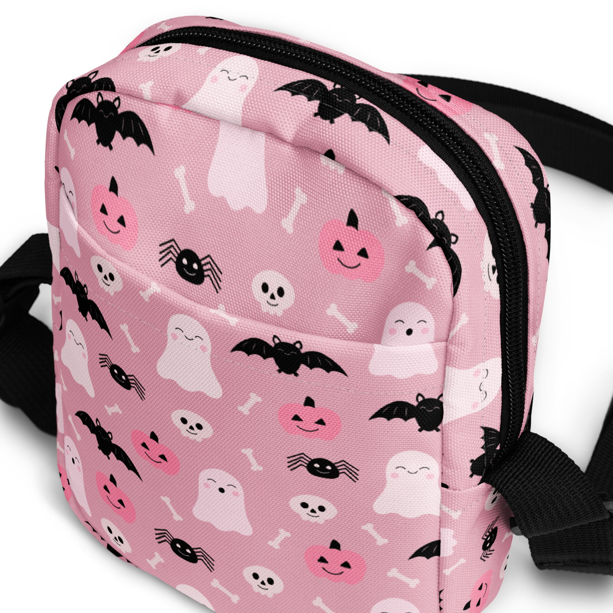 Pink halloween crossbody purse for girls with black zippers and straps featuring white and black ghost and bat patterns