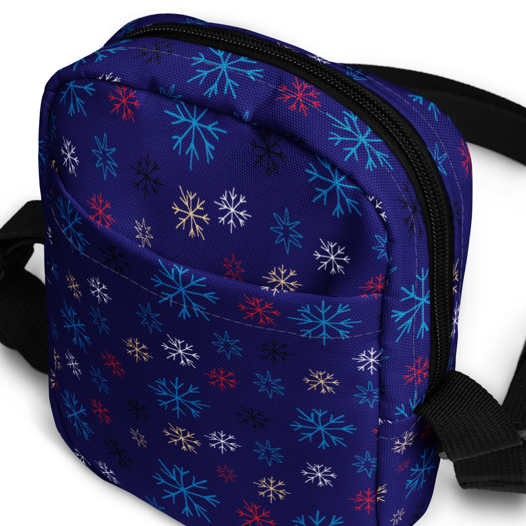 A navy blue girls crossbody purse with a vibrant multicolor snowflake pattern in red white teal and gold