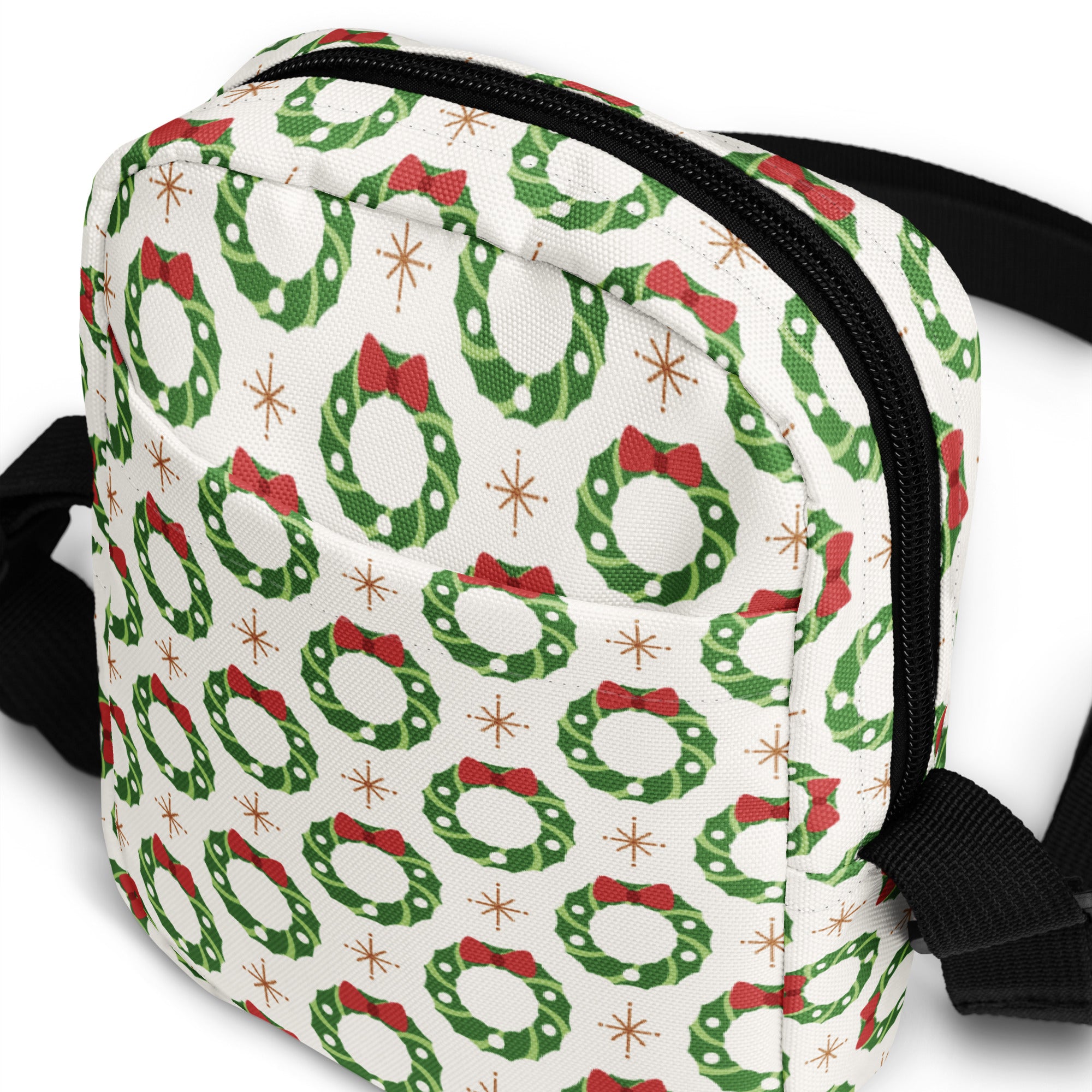 White girls Christmas wreath crossbody purse with green wreaths red bows and gold starbursts on fabric surface