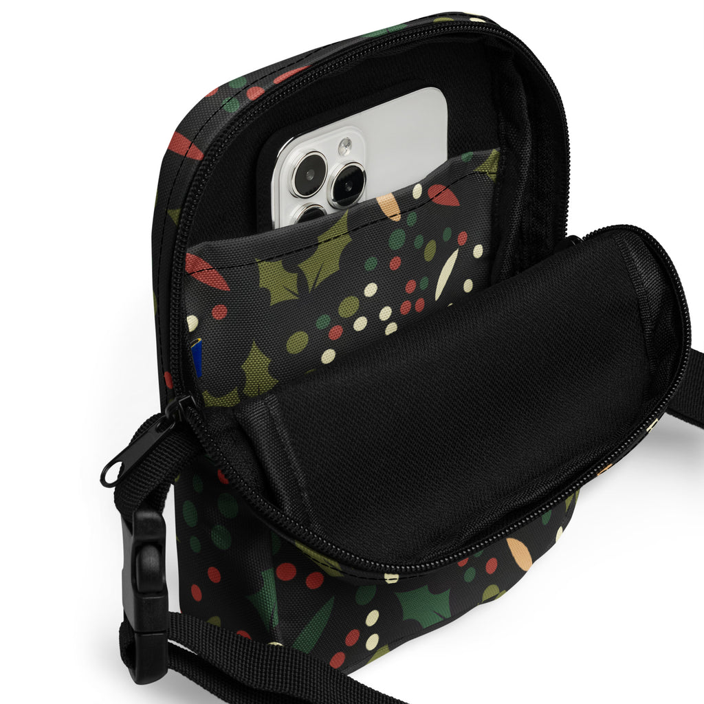 Black crossbody phone pouch with festive holiday pattern of green holly leaves red berries and multicolored polka dots