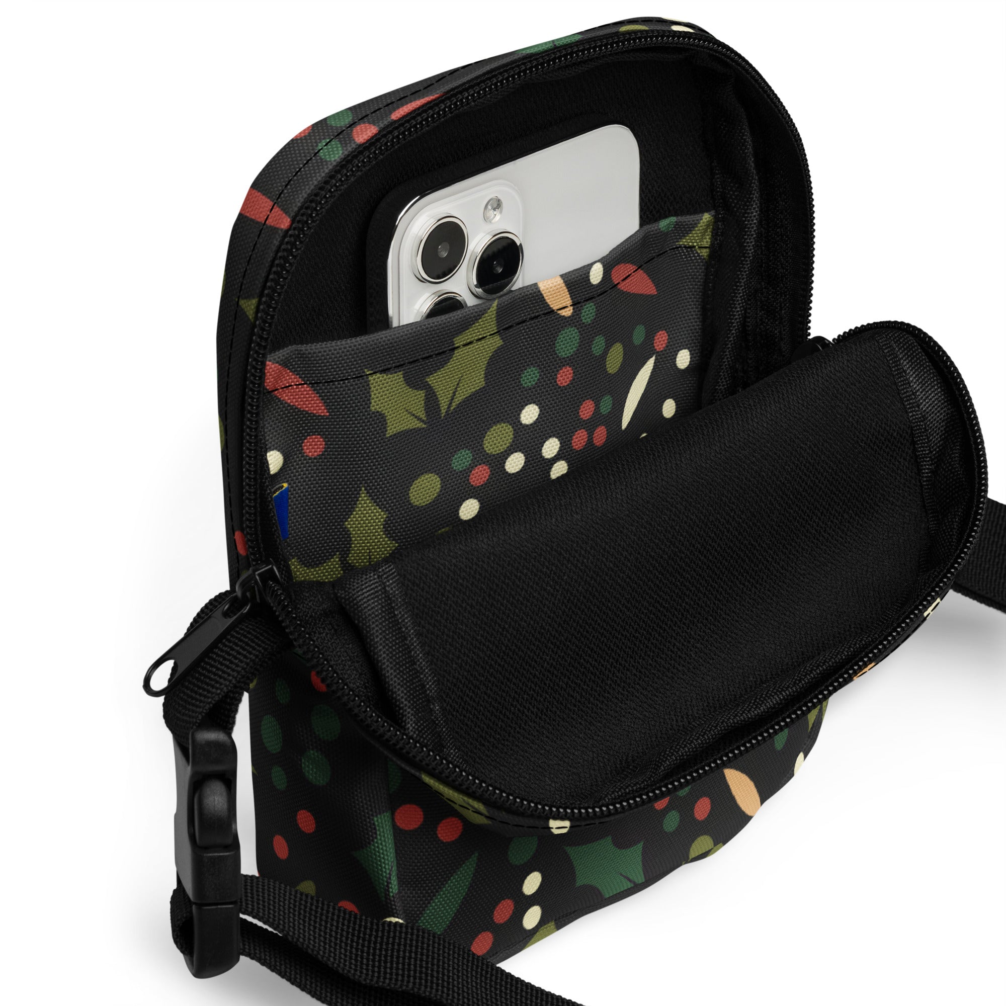 Black crossbody phone pouch with festive holiday pattern of green holly leaves red berries and multicolored polka dots