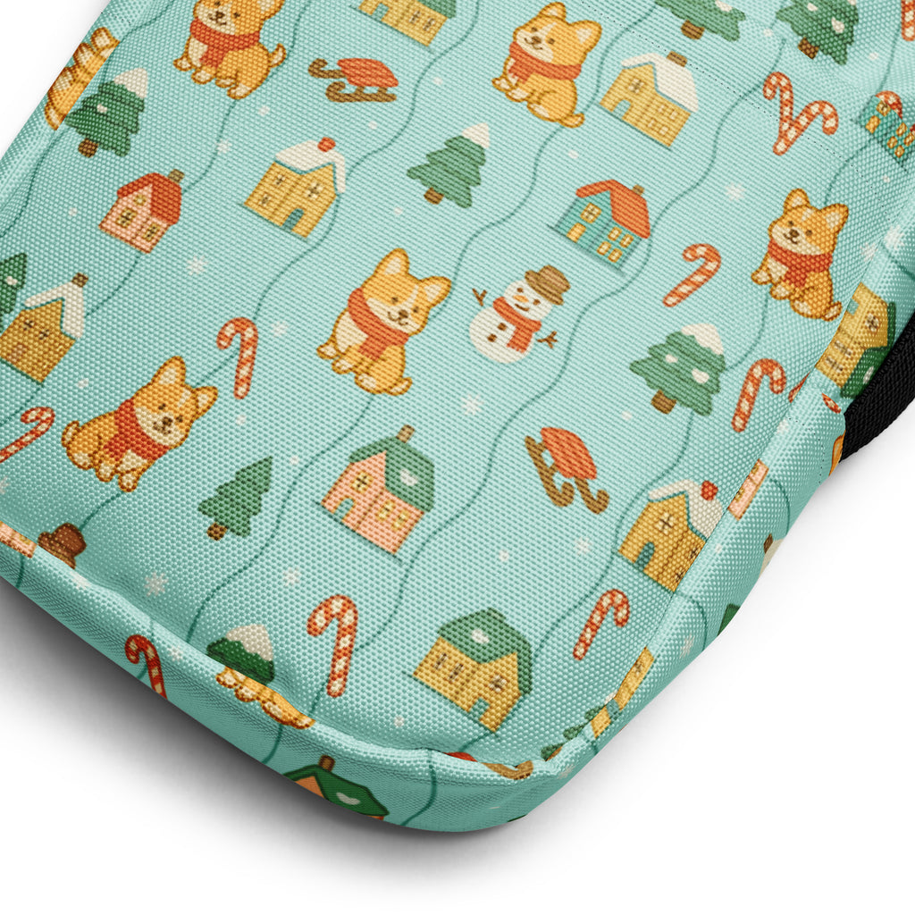 A teal fabric crossbody purse featuring a festive pattern of cartoon corgis snowmen candy canes and houses