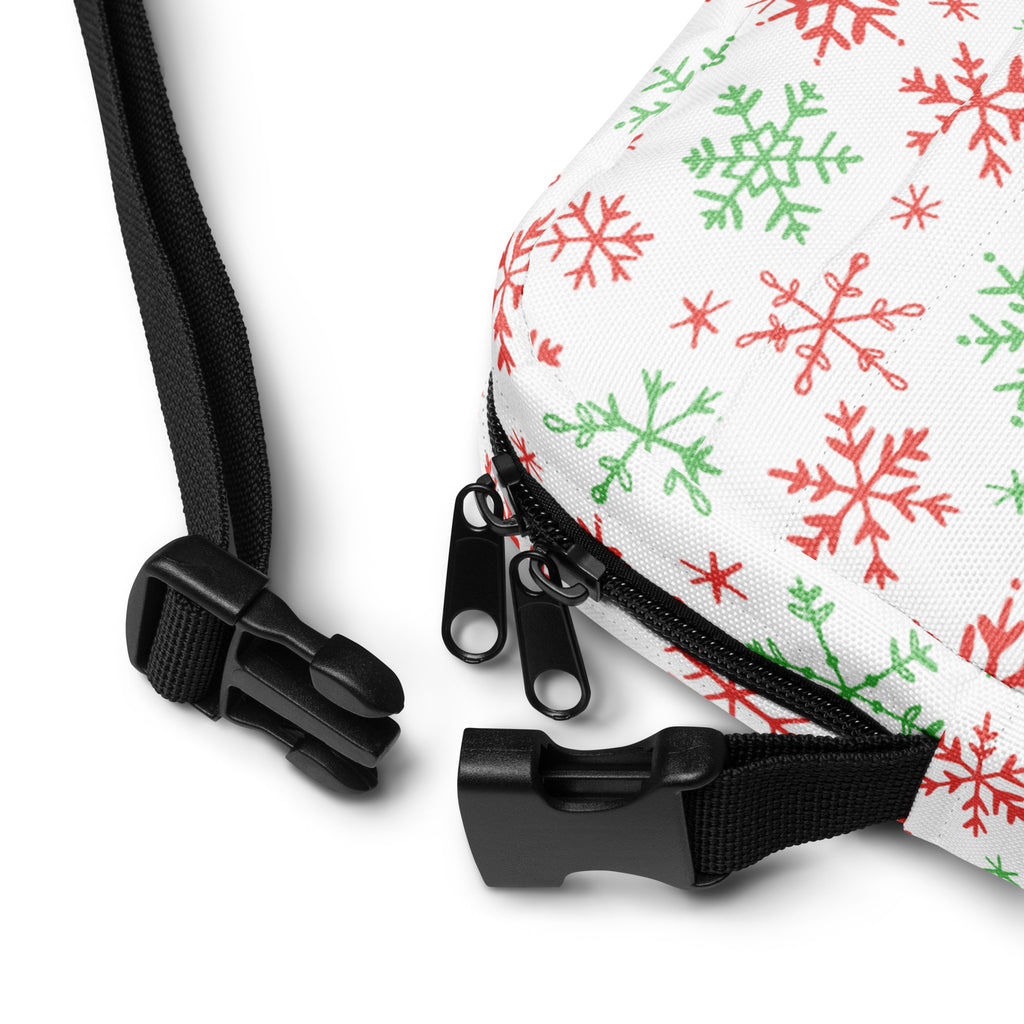 White crossbody bag with red and green snowflake patterns featuring black zippers and adjustable strap hardware