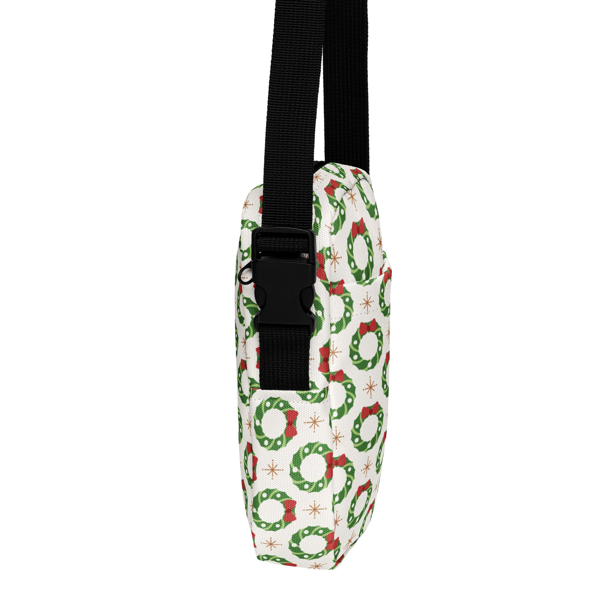 White crossbody bag with green wreaths and red bows print on fabric featuring black adjustable strap and buckle