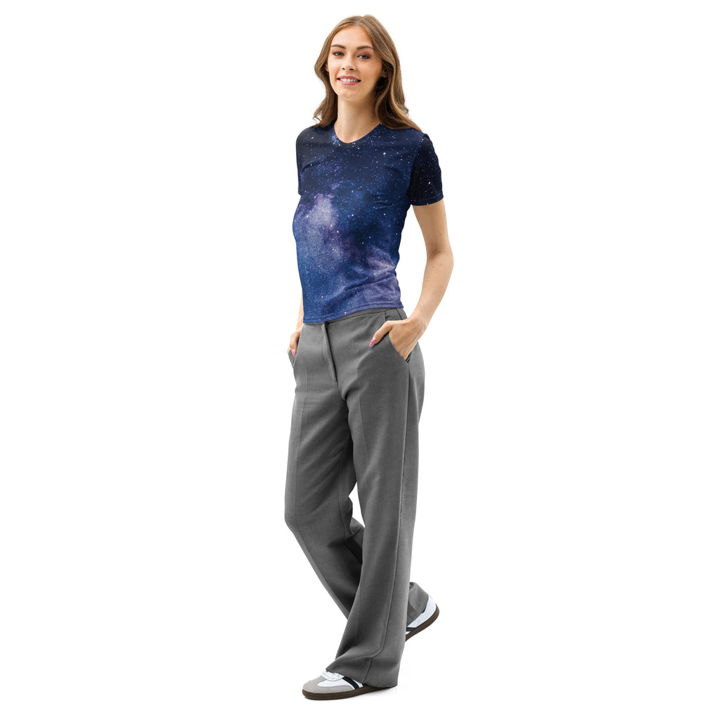 A woman wearing a women’s realistic galaxy cotton t-shirt with deep blue and purple cosmic print paired with gray pants